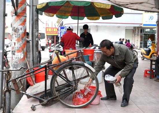 一名賣卷筒粉的攤主在廣西橫縣橫州鎮街頭將不同的垃圾分類投放到4個垃圾袋里(4月13日攝)。 新華社記者 周華 攝